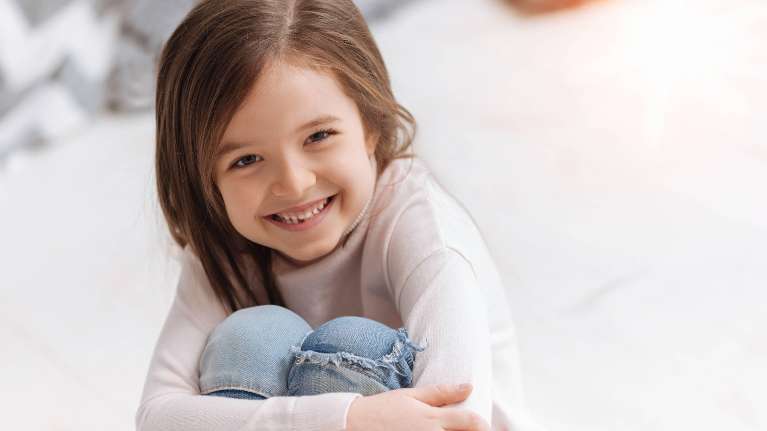 A smiling child hugging her knees